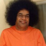 shri sathya sai baba in orange attire with curly hair.