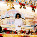 Sathya Sai Baba standing amidst Christmas decorations.