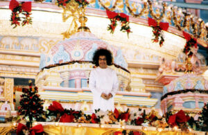 Sathya Sai Baba standing amidst Christmas decorations.