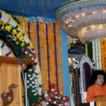 A man speaking while Sathya Sai sits.
