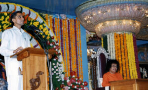 A man speaking while Sathya Sai sits.