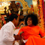 Shri Sathya Sai Baba blessing devotee near Krishna idol