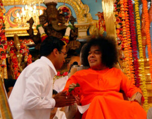 Shri Sathya Sai Baba blessing devotee near Krishna idol