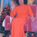 Shri Sathya Sai Baba sitting on chair raising hand