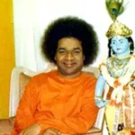 Sathya Sai Baba sitting beside Krishna statue.