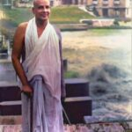 Swami Sivananda standing peacefully beside riverside retreat building