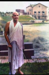 Swami Sivananda standing peacefully beside riverside retreat building