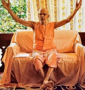 Hindu monk raising both hands while delivering spiritual discourse indoors