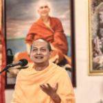 Hindu monk delivering a spiritual discourse before a portrait of Swami Sivananda