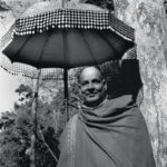 Swami Sivananda standing beneath umbrella in peaceful forest