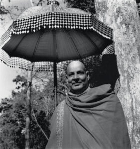 Swami Sivananda standing beneath umbrella in peaceful forest