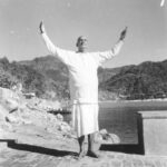 Swami Sivananda raising hands beside sacred river