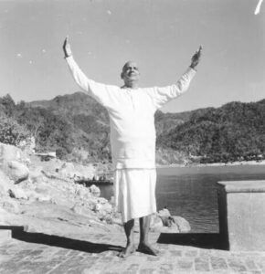 Swami Sivananda raising hands beside sacred river