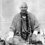 Swami Sivananda seated with flower garland smiling peacefully