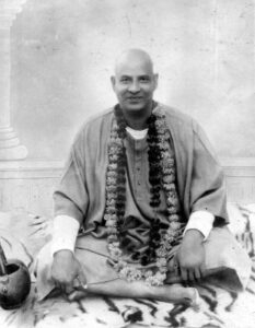 Swami Sivananda seated with flower garland smiling peacefully