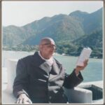 Swami Sivananda sitting outside and reading book.