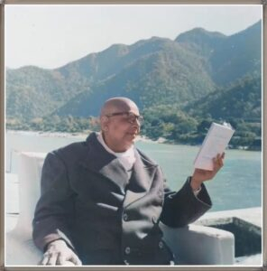 Swami Sivananda sitting outside and reading book.