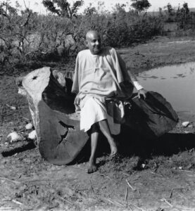 Swami Sivananda sitting on a fallen tree trunk
