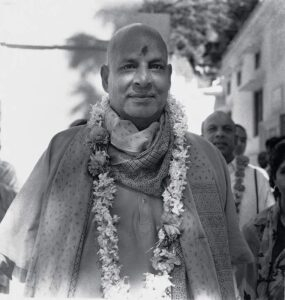 Swami Sivananda wearing flower garland smiling peacefully outdoors