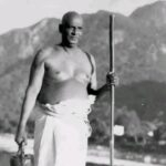 Swami Sivananda standing holding a wooden staff.