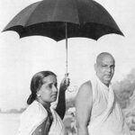 Woman holding an umbrella over Swami Sivananda.