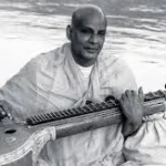 Swami Sivananda playing veena beside the Ganges