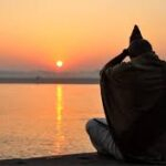 Meditating devotee watching the sunrise by river