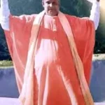 Swami Sivananda standing outdoors holding hand cymbals during devotional singing