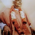 Swami Sivananda wearing flower garland seated peacefully in devotional contemplation