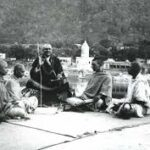 Swami Sivananda teaching disciples outdoors beside sacred river with peaceful guidance