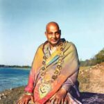 Spiritual guru meditating beside riverside wearing sacred shawl and garlands