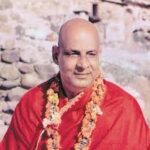 Spiritual guru wearing red robes and flower garland peacefully seated