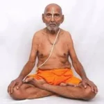 Sri Swami Sivananda seated in lotus meditation posture with calm spiritual expression