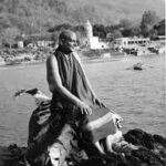 Swami Sivananda meditating beside sacred riverbank peacefully