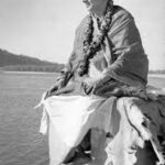 Swami Sivananda meditating beside peaceful riverside landscape