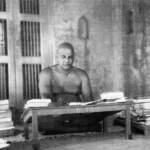 Swami Sivananda studying sacred scriptures surrounded by books and spiritual literature