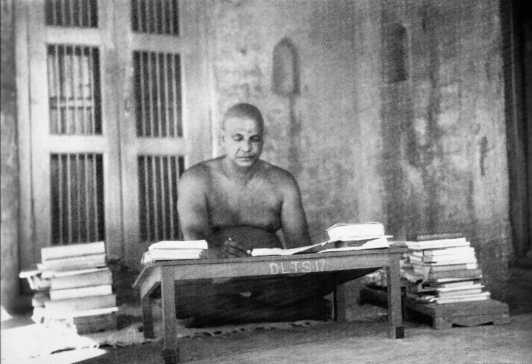 Swami Sivananda studying sacred scriptures surrounded by books and spiritual literature