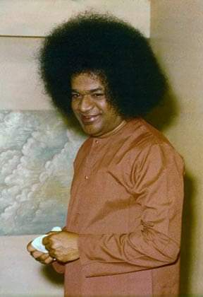 Sri Sathya Sai Baba smiling gently while holding sacred object indoors