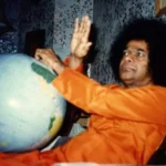 Bhagawan Sri Sathya Sai Baba blessing beside a world globe