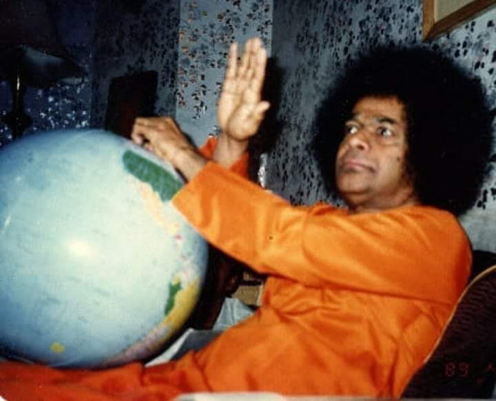 Bhagawan Sri Sathya Sai Baba blessing beside a world globe