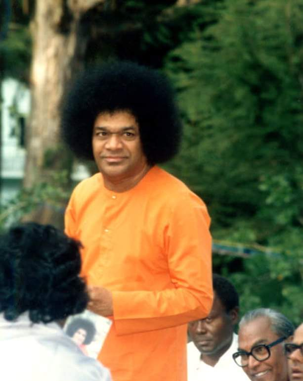 Bhagawan Sri Sathya Sai Baba smiling among devotees in lush greenery